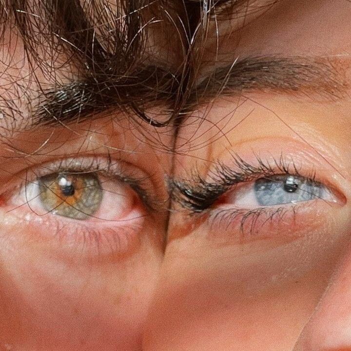 An artistic close-up of two faces together, showing one hazel-green eye and one blue eye.